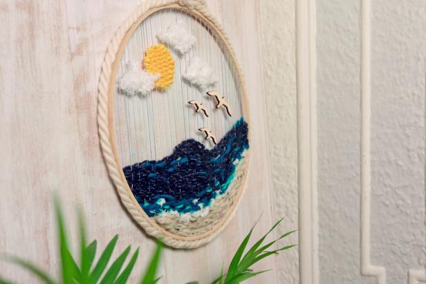 Embroidery hoop and yarn wreath with beach scene hangs on wall
