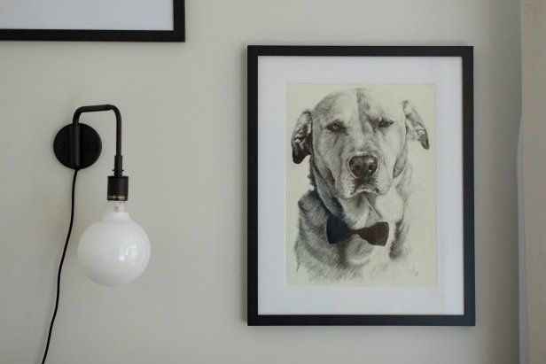 A matte metal globe sconce is placed next to artwork featuring the homeowner's dog.