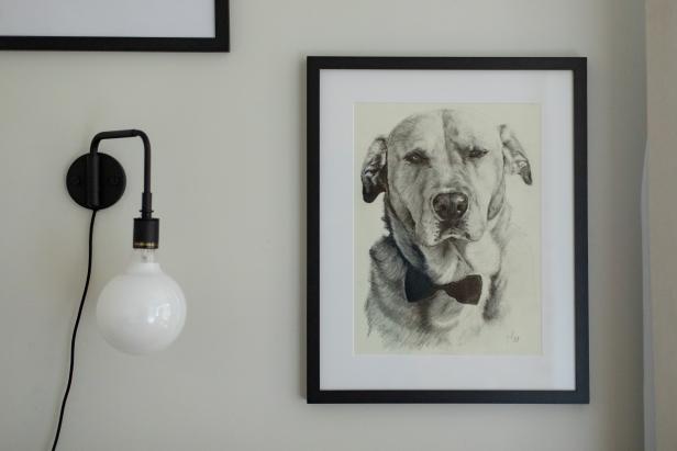 A matte metal globe sconce is placed next to artwork featuring the homeowner's dog.