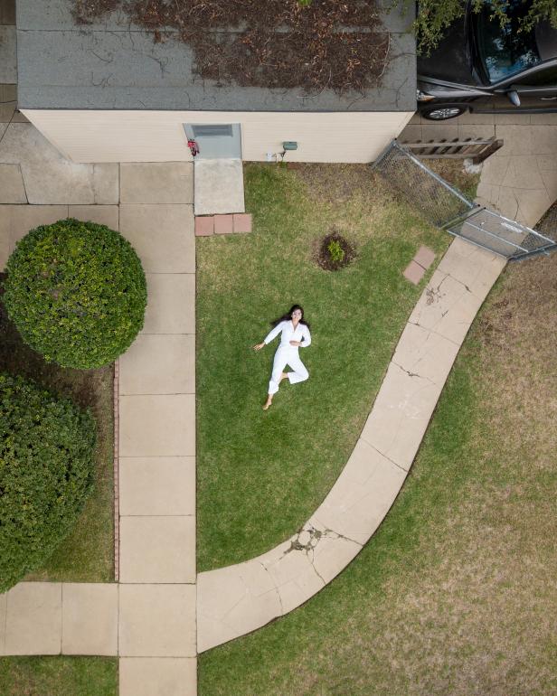 A woman in a white jumpsuit shot from above on a green lawn.