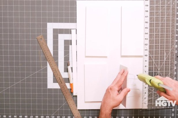 Using a crafting knife, carefully cut the white foam board 13’’ across. For accuracy, measure the foam board using a ruler. Then, cut four smaller rectangles for the door panels. Next, lightly trace out where each panel will go on the door and then use a low temp hot glue gun to adhere three of the panels to the door.