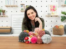 Woman Poses With Fluffy Pom-Poms at Crafting Work Bench