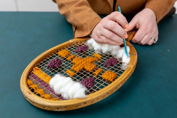 Using a crochet hook, push the thick wool through the squares of the racket.