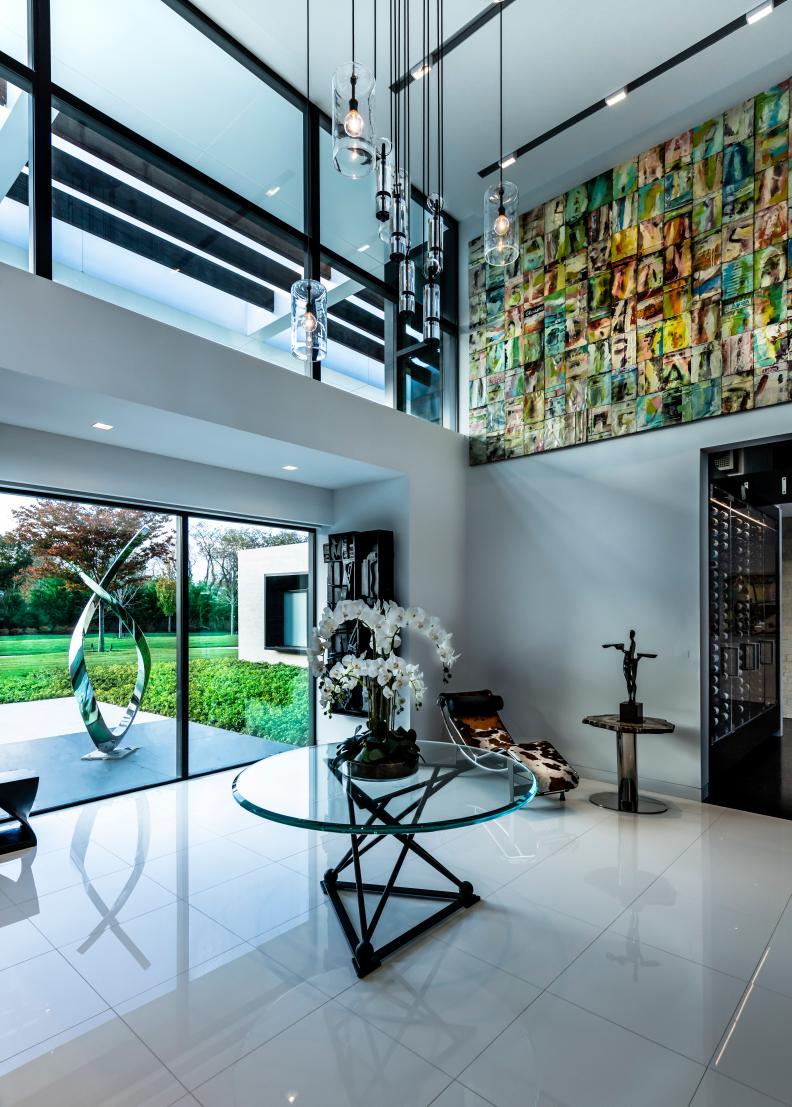 A modern white foyer features colorful art and a glass table.