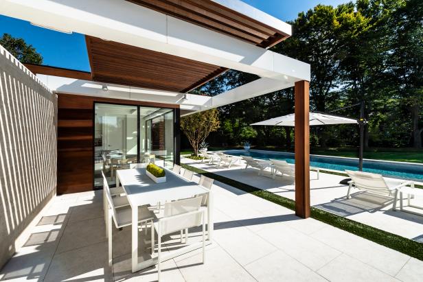 White powder-coated dining pieces sit under a mahogany pergola.