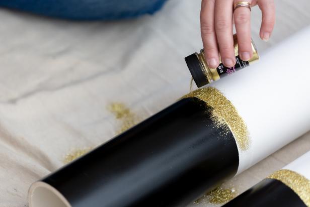 Glitter is sprinkled onto a strip of decoupage glue on a PVC pipe that has been painted to resemble the leg of a giant nutcracker Christmas decoration.