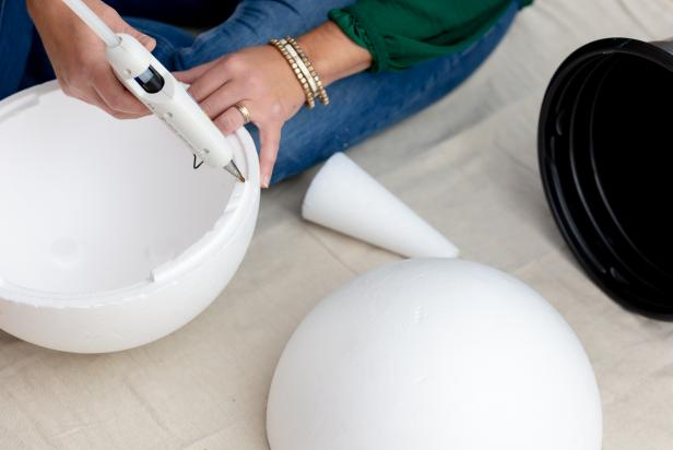 Hot glue is used to secure two halves of a giant foam ball together for the head of a giant nutcracker Christmas decoration.