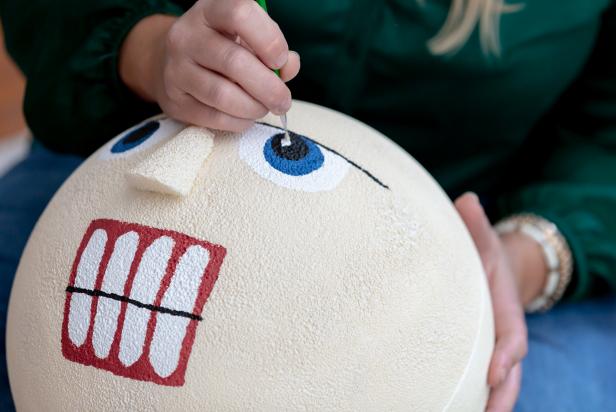 Paint is used to add the facial features to the large foam ball that is used as the head on this giant DIY nutcracker decoration.
