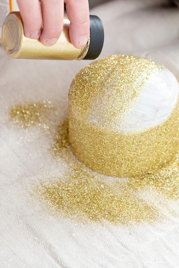 Glitter is sprinkled onto a piece of PVC that has been coated with a layer of decoupage glue for a DIY Christmas decoration.