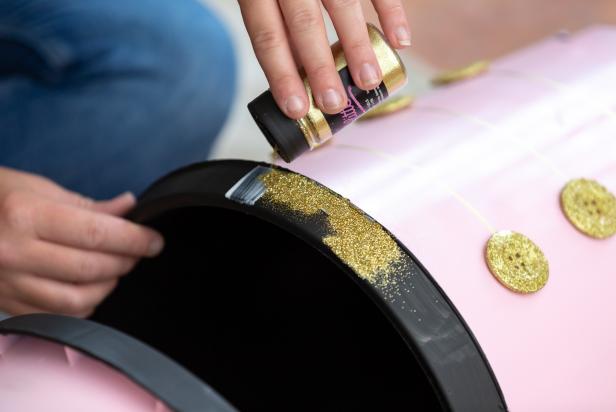 Glitter is sprinkled onto a layer of decoupage glue that has been painted onto a plastic planter as part of a DIY nutcracker Christmas decoration.