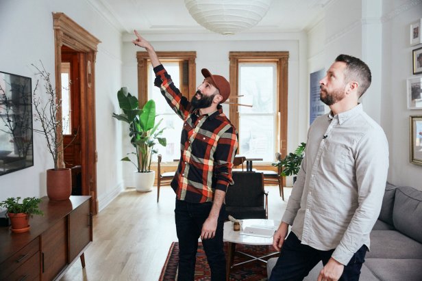 Two Men Stand in Living Room, One Pointing at Ceiling in New York Home