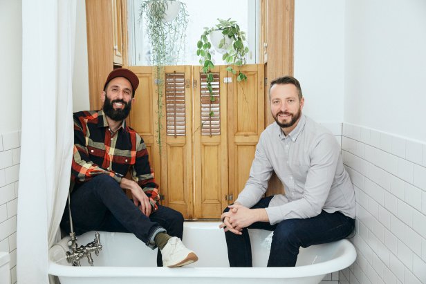 Two Men Pose for Camera Inside Clawfoot Tub in Renovated Bath