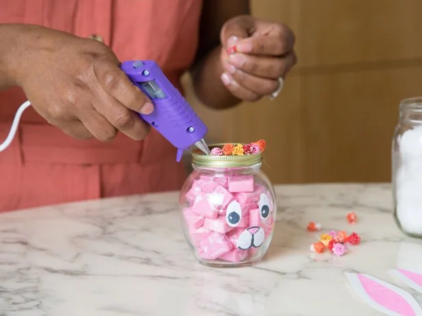 These candy wrappers have been folded and rolled to look like flowers and then glued to the top of a jar full of candy that has been painted to look like a bunny.