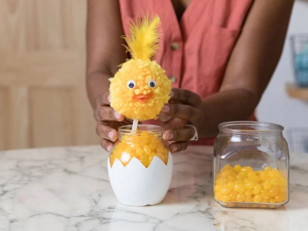 This jar has been painted and decorated to look like a chick hatching from an egg and then filled with yellow candy. The chick is made from a pompom and placed in the candy using a popsicle stick.