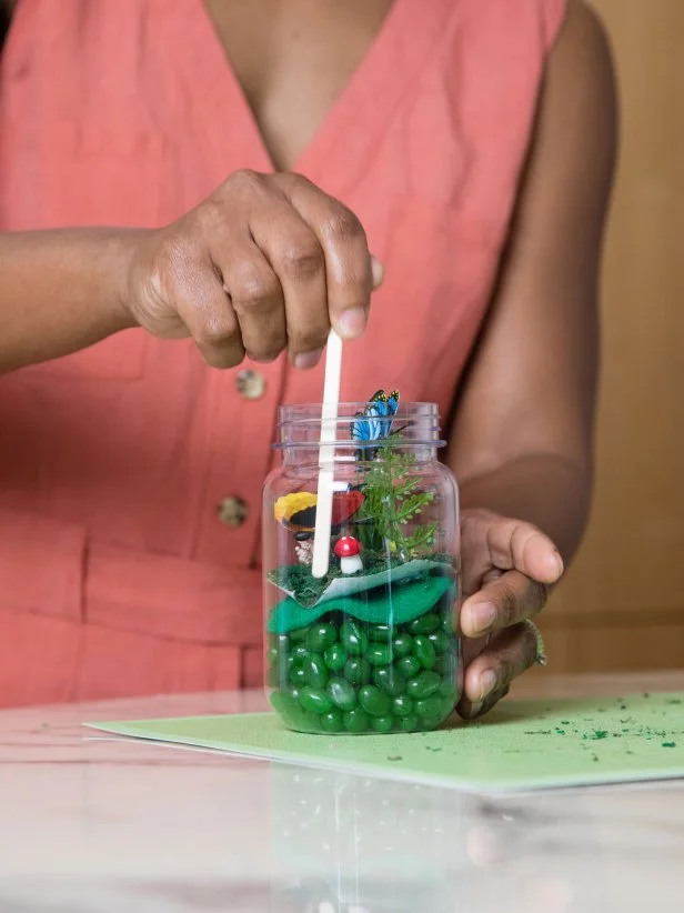 A popsicle stick is used to manipulate items inside of a glass jar full of candy.