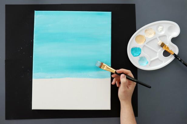 Paint the top two-thirds of your canvas light blue with a 1” flat brush. Using the same brush, add streaks of teal paint on top and blend the colors together. Be sure to paint the edges of your canvas as well.
