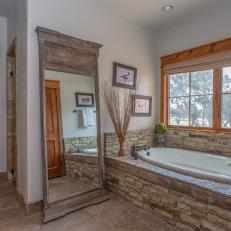 Peaceful Master Bathroom With Gorgeous Floor Mirror and Stone-Wrapped Bathtub