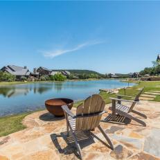 Stone Patio With Metal Fire Basin and Wood Adirondack Chairs Beside a Private Lake