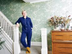 Woman Stands at Base of Stairs With Vintage Floral Wallpaper Behind