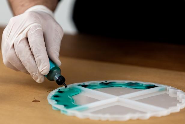 Pour a thin layer of the teal resin around the outside edge of your chosen mold. Add a couple of drops of the teal alcohol ink directly into your first pour and mix with a wooden skewer.