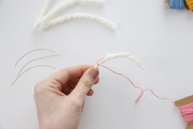 Tie embroidery thread onto the yarn, making sure it’s around the wire as well. Wrap the thread around the yarn, covering up the tail end as you go. Continue until the wrapped portion measures 1¾”, then tie off the string and trim the excess.