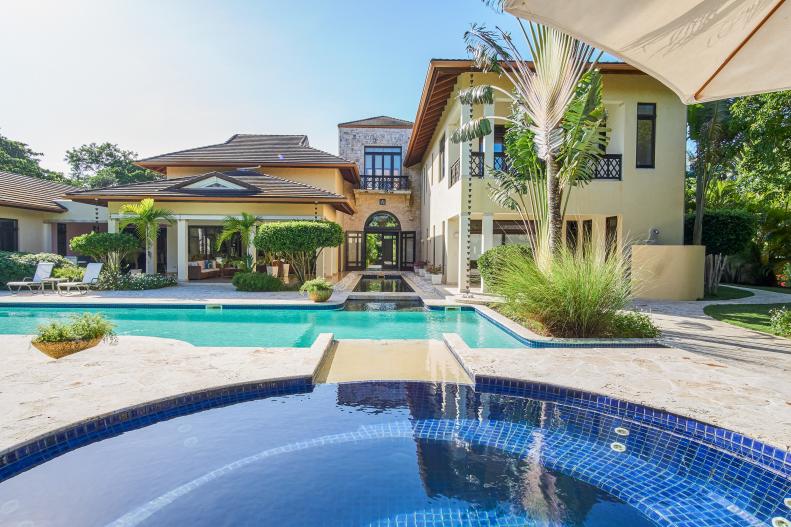 A Swimming Pool and a Flagstone Patio Sits Near a Tropical Villa 