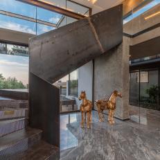 Iron-Sided Staircase Is Featured in a Window-Filled Foyer With a Set of Bronze Statues 