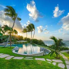 Palm Trees and a Stone Walkway Surround a Waterfront Swimming Pool