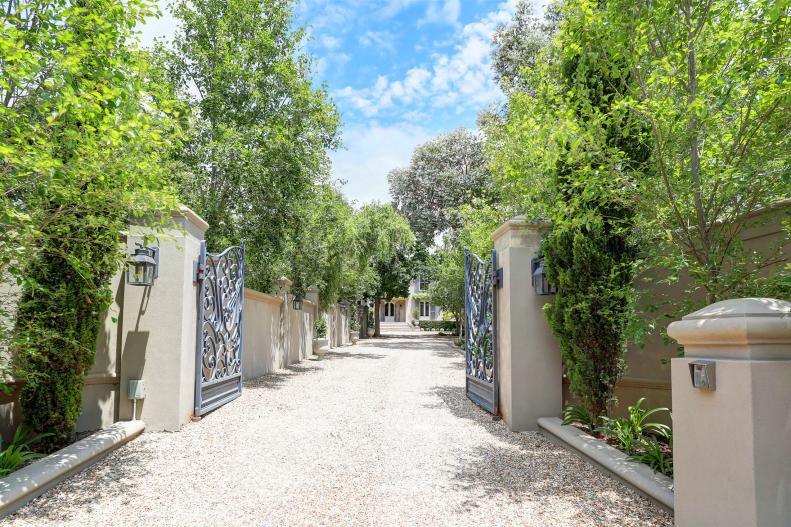 A Gravel Driveway Is Lined With Stone Pillars and Feature Iron Gates