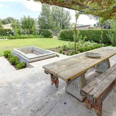 Stone Covered Patio With a Canopy of Vines Features a Wood Picnic Table and 
