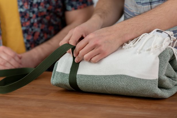 Roll up the blanket. Measure by wrapping a piece of nylon strap around it, leaving a 2-inch overhang. For this blanket, cut two 10-inch pieces of nylon. Then, measure out and cut two nylon straps to carry the blanket. Cut one the exact size of the width, and cut the other just a little bit longer.