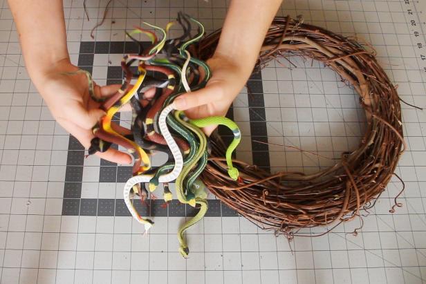 Weave the snakes into the wreath, starting with the larger snakes. Use hot glue to hold the snakes down if needed, but they should mostly stay in place just by weaving them through the sticks of the wreath.