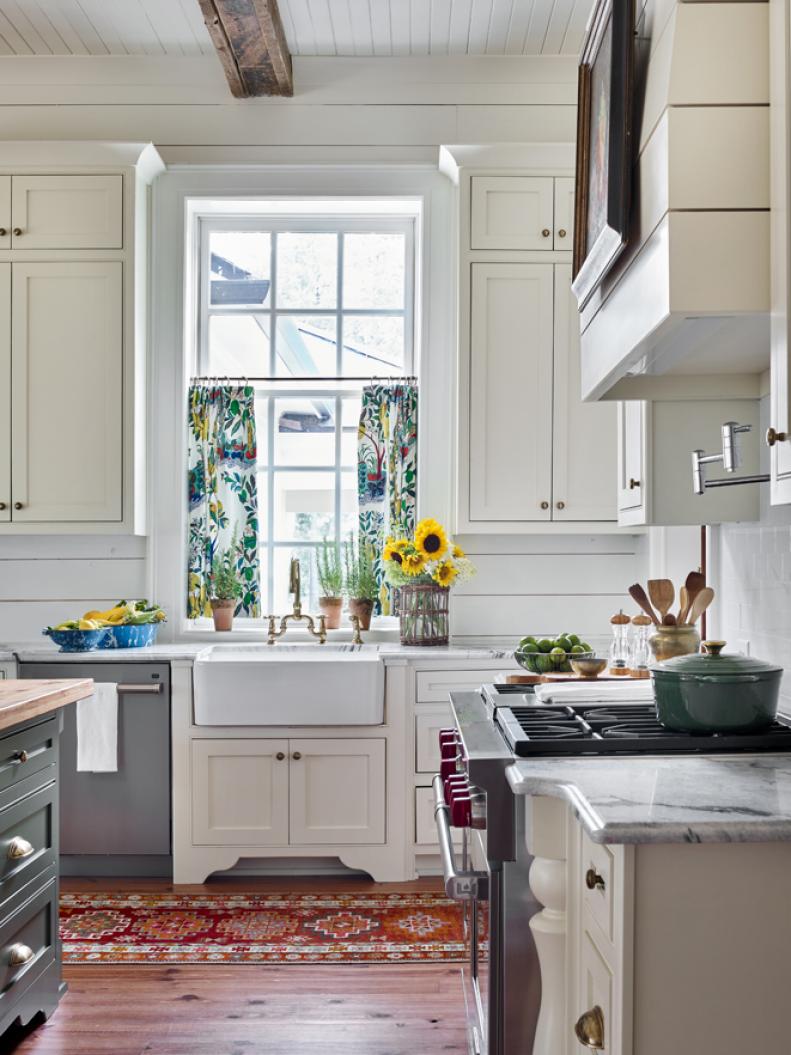 Colorful curtains flank a window above a white farm sink in a kitchen.