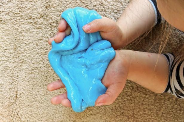 A child cradles blue slime in both hands above beige carpet.
