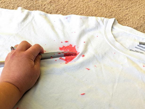 A left hand uses a butterknife to scrape red slime from a t-shirt. 