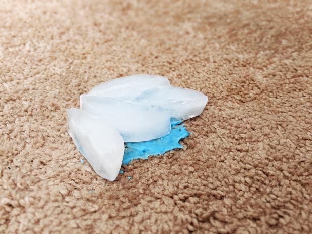 Four ice cubes sit on top of a blue slime stain on beige carpet