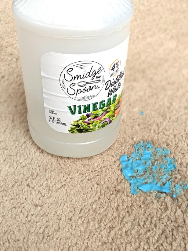 A bottle of vinegar sits to the left of a blue slime stain on carpet