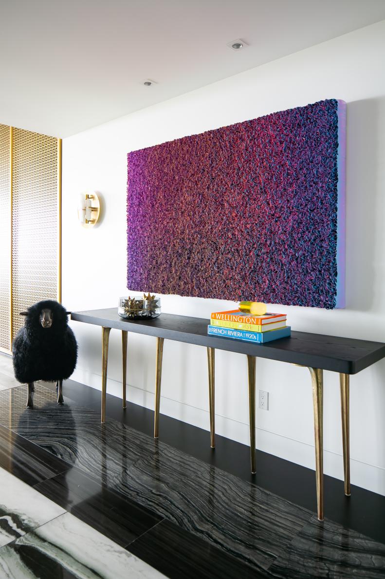 Black and Gold Console Table Sits Below a Colorful Piece of Modern Art
