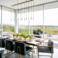 Modern Dining Room With Walls of Windows Features a Gold Chandelier and a Wood Slab Table