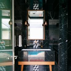 Small Powder Room Features Black Marble Walls and Flooring and a Midcentury Modern Vanity