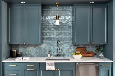 Stacked brown kitchen cabinets flank a black range hood mounted to white  subway backsplash tiles over a stai…