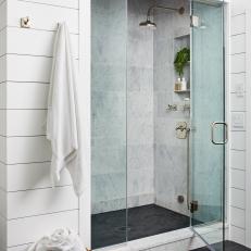 Bright Bathroom Features a Glass Walk-In Shower With Marble Wall Tile and Black Floor Tile