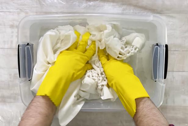 Then, wearing rubber gloves, place your shower curtain into the plastic tub filled with water.