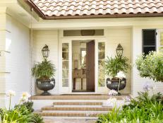 A white brick cottage has palmettos in urns on either side of the door.
