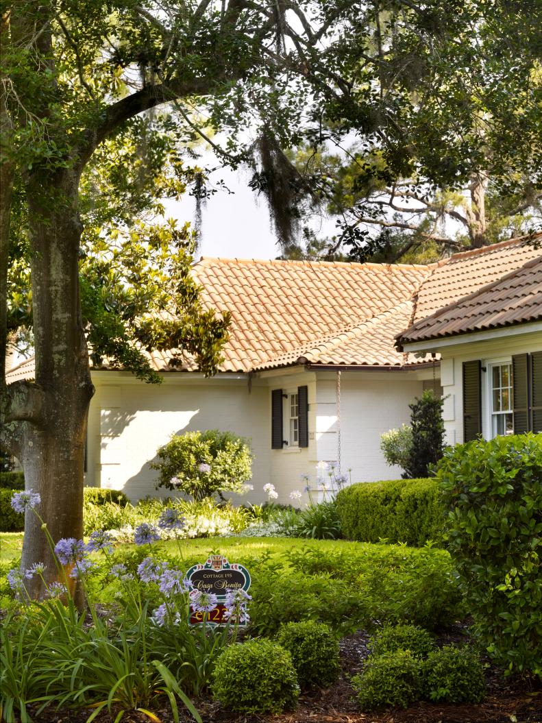 A white brick cottage with a terra cotta roof among trees.