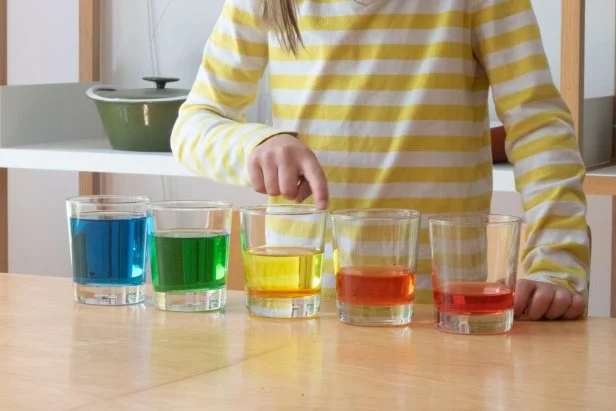 A child uses a glass harp made from barware and rainbow colored water.
