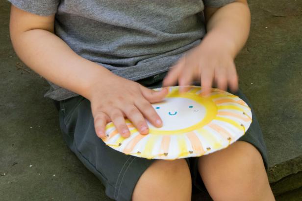 A preschooler tapping on a painted paper plate drum.