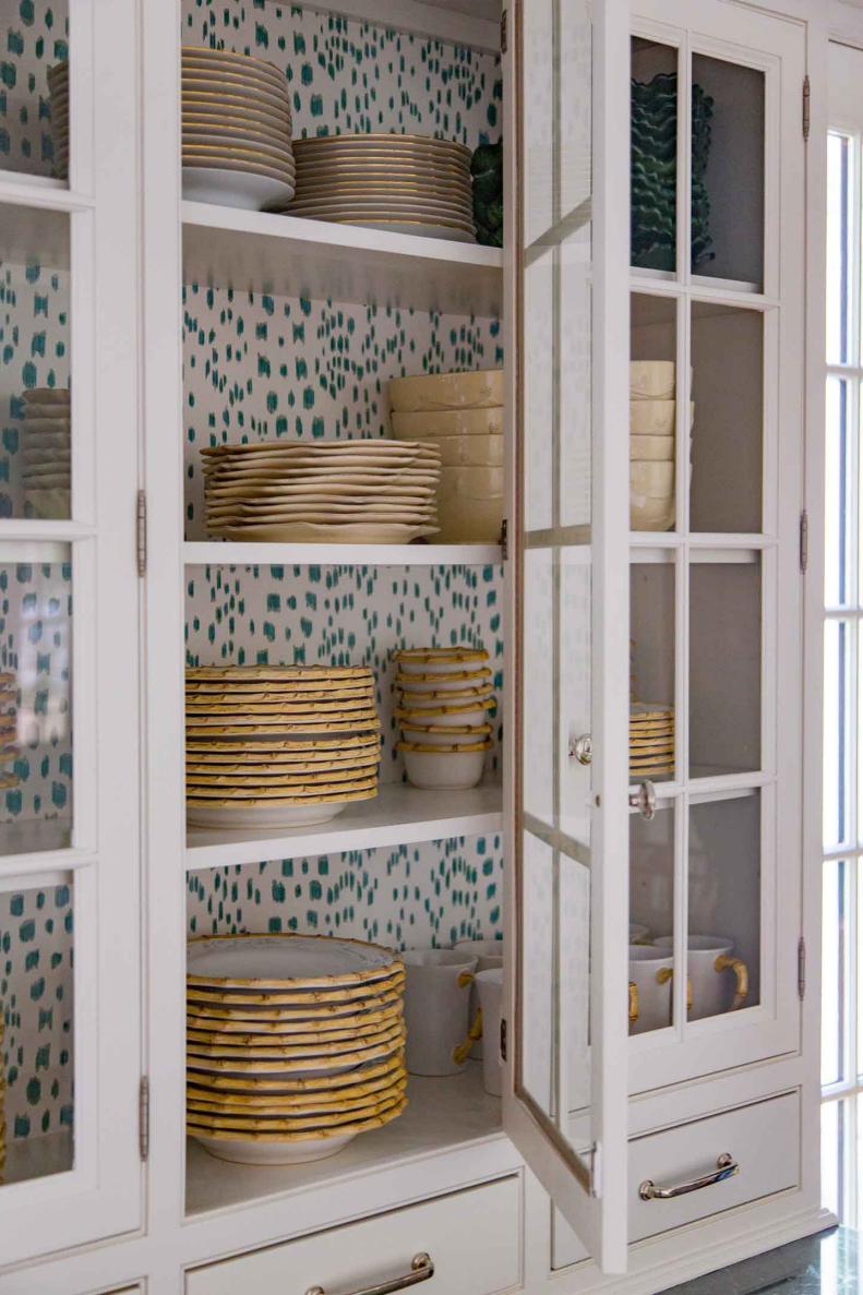 A white glass-fronted cabinet is lined with spotted wallpaper.
