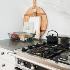 Gray Cabinets Surround a Gas Range That Sits in Front of a Marble Slab Backsplash