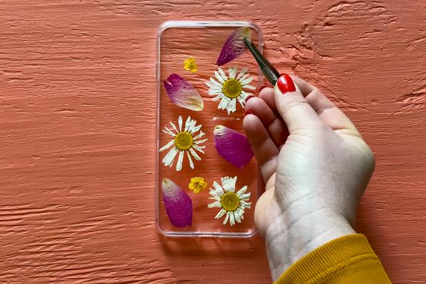 Using tweezers, arrange the petals and flowers into a design on the cell phone case.